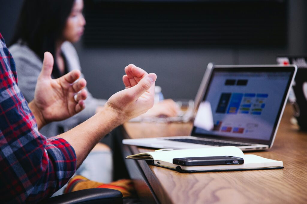 Personen in einem Meeting diskutieren und arbeiten an einem Laptop, während eine Person gestikuliert - Digitale Transformation im Gesundheitswesen